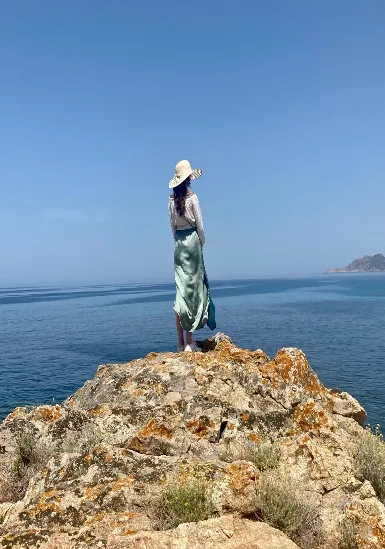 Anne steht auf einem Felsen am Meer und blickt in die Weite
